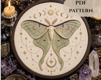 May include: A detailed embroidery hoop art piece featuring a large moth with green and gold wings, surrounded by celestial designs. The artwork is set against a cream-colored fabric, framed in a dark wooden hoop. The text "PDF PATTERN" is visible.