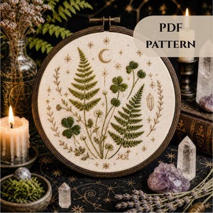 Peut inclure: Broderie sur tambour représentant un motif botanique avec des fougères, des trèfles et un croissant de lune. L'œuvre est dans un cercle en bois et comprend le texte "PDF PATTERN". La palette de couleurs comprend le vert, le beige et le marron.