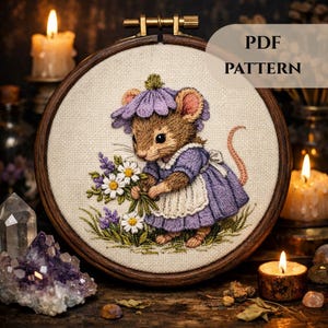 Könnte beinhalten: Detaillierte Stickerei einer Maus in einem lila Kleid und Hut, die einen Strauß Gänseblümchen und lila Blumen hält. Die Stickerei befindet sich in einem Holzrahmen, mit dem Text "PDF PATTERN". Der Hintergrund ist dunkel mit brennenden Kerzen.