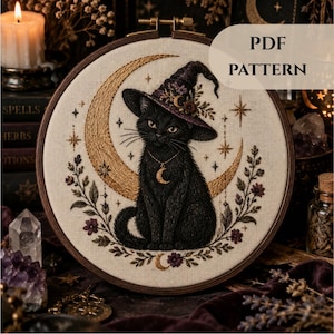 May include: An embroidery hoop containing a fabric piece with a stitched black cat wearing a purple witch hat, positioned in front of a gold crescent moon. The design includes floral accents, stars, and a moon pendant necklace. Text reads PDF PATTERN.