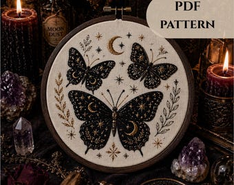 May include: An embroidery hoop featuring a celestial butterfly design. The butterflies are black with gold star and moon details, set against a cream-colored fabric. The text "PDF PATTERN" is at the top. The wooden hoop is surrounded by candles and crystals.