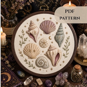 Puede incluir: Patrón de conchas bordadas en un aro de madera. El diseño presenta varias conchas en tonos beige, rosa y azul, con detalles dorados y el texto "PDF PATTERN".