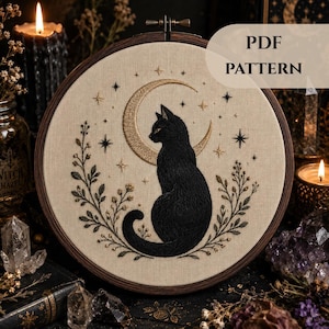 May include: An embroidery hoop containing a fabric panel with a black cat silhouette stitched in the center, framed by a gold crescent moon and stars, with floral sprigs on both sides. The text PDF PATTERN is printed in the upper right corner.