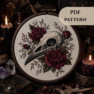 May include: An embroidery hoop containing a fabric piece with a stitched bird skull surrounded by deep red roses and green leaves. The text PDF PATTERN is visible in the upper right corner. The design features intricate needlework on off-white fabric.
