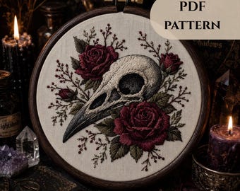 Peut inclure: Un tambour à broder contenant une pièce de tissu avec un crâne d'oiseau brodé entouré de roses rouge foncé et de feuilles vertes. Le texte PDF PATTERN est visible dans le coin supérieur droit. Le motif présente une broderie complexe sur tissu écru.