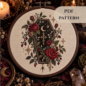 May include: An embroidery hoop containing a fabric piece with a stitched design of a black coffin adorned with red roses, green leaves, a gold crescent moon, and a gold cross. The design includes small gold stars and the text PDF PATTERN.