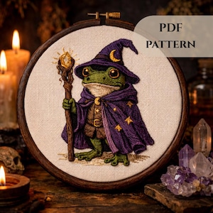 Może przedstawiać: Szczegółowy haft na tamborku przedstawiający zieloną żabę ubraną jako czarodziej, w fioletowym kapeluszu i pelerynie ze złotymi gwiazdami. Żaba trzyma laskę z błyszczącym kryształem. Widoczny tekst "PDF PATTERN". Ciemne, klimatyczne tło.