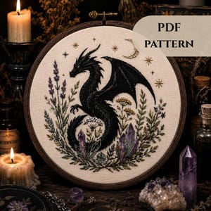 May include: Embroidered dragon pattern in a wooden hoop. The black dragon is surrounded by purple lavender, crystals, and other foliage. The text "PDF PATTERN" is visible on the top right.