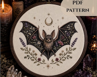 Puede incluir: Un bastidor de bordado circular que contiene una pieza de tela con una ilustración detallada de un murciélago, con alas extendidas adornadas con bordados florales coloridos, una luna creciente y estrellas. El texto PDF PATTERN aparece arriba.