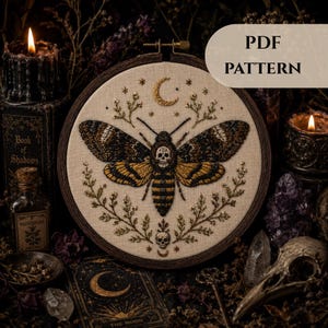 Könnte beinhalten: Ein Stickrahmen mit einem Stoffstück, auf dem eine Motte mit einem Totenkopfmuster auf dem Thorax gestickt ist. Das Design umfasst eine Mondsichel, Sterne, florale Zweige und einen kleinen Totenkopf. Der Text lautet PDF PATTERN.