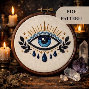 Puede incluir: Diseño de ojo bordado en un aro de madera. El ojo es azul con detalles dorados y negros, rodeado de hojas y lágrimas. El texto "PDF PATTERN" se muestra en la parte superior derecha. El fondo incluye velas y cristales.