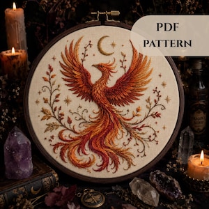 May include: A detailed embroidery pattern featuring a phoenix with outstretched wings, rendered in shades of orange and red. The design includes a crescent moon and stars, set within a wooden hoop. The text "PDF PATTERN" is visible.