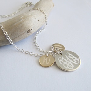 May include: A silver chain necklace with three charms. Two of the charms are round and gold with a single letter engraved on each. The third charm is larger and silver with a monogram engraved on it.
