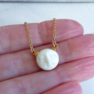 May include: A gold chain necklace with a white ceramic pendant featuring a carved face.