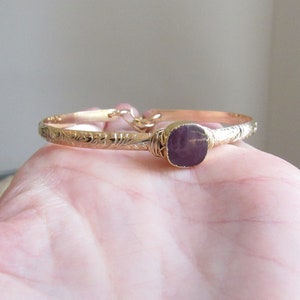 May include: A gold bangle bracelet with an engraved floral design and a purple gemstone set in the centre.
