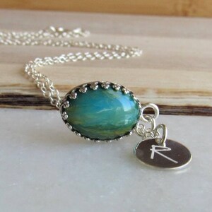 May include: A silver chain necklace with a blue and green oval pendant and a silver charm with the letter 'R' engraved on it.