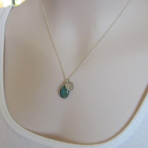 May include: A silver chain necklace with a green oval pendant and a small silver charm with the letter 'R' engraved on it.