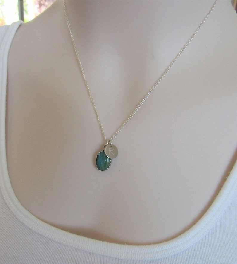 May include: A silver chain necklace with a green oval pendant and a small silver charm with the letter 'R' engraved on it.
