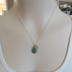 May include: A silver chain necklace with a green oval pendant and a small silver charm with the letter "R" engraved on it.