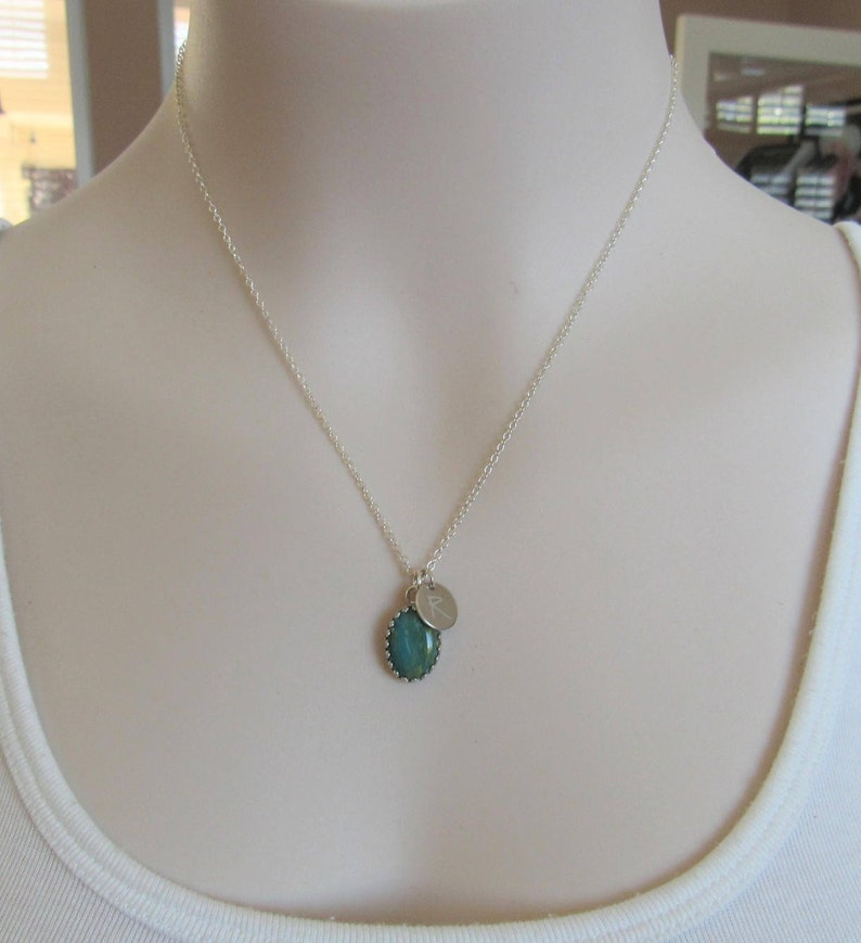 May include: A silver chain necklace with a green oval pendant and a small silver charm with the letter "R" engraved on it.