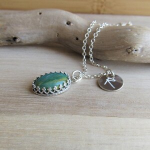 May include: A silver chain necklace with a green and brown oval stone pendant set in a silver crown design. A small silver charm with the letter 'R' is attached to the chain.