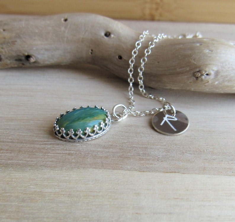 May include: A silver chain necklace with a green and brown oval stone pendant set in a silver crown design. A small silver charm with the letter 'R' is attached to the chain.