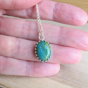 May include: A silver chain necklace with a green and yellow oval pendant. The pendant has a silver bezel setting with a scalloped edge.