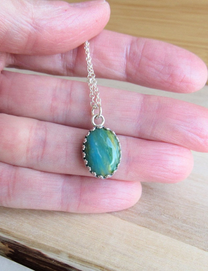 May include: A silver chain necklace with a green and yellow oval pendant. The pendant has a silver bezel setting with a scalloped edge.