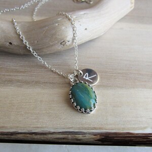May include: A silver chain necklace with a green and brown oval stone pendant and a silver charm with the letter "R" engraved on it.