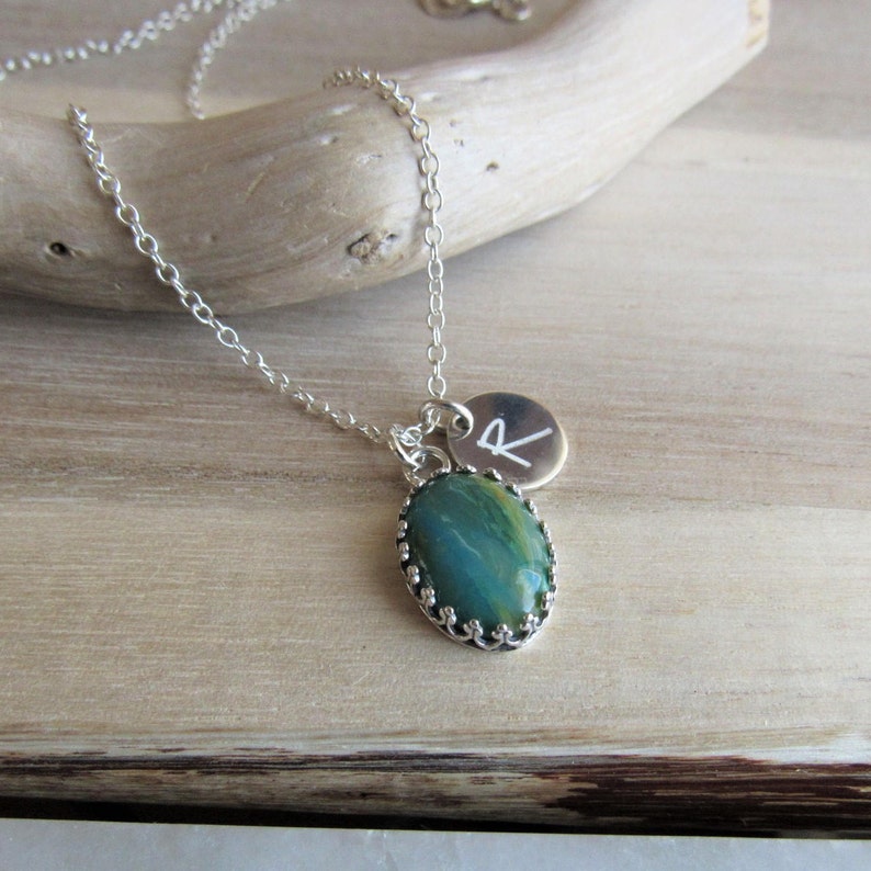 May include: A silver chain necklace with a green and brown oval stone pendant and a silver charm with the letter "R" engraved on it.