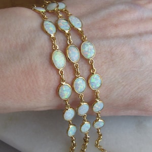 May include: Three gold-toned bracelets with oval-shaped opals. Each opal is set in a gold bezel and linked by delicate gold chains. The bracelets have lobster claw clasps for secure fastening. The opals display a play of color.