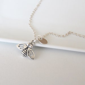 May include: A silver chain necklace with a small silver bee charm and a silver disc pendant.