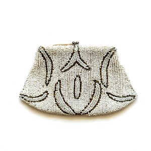 May include: A white beaded clutch purse with a geometric design. The purse is made of small, white beads and has a silver clasp.