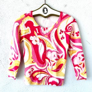 May include: A pink and yellow long-sleeved shirt with a paisley pattern and rhinestones. The shirt has a scoop neck and three-quarter sleeves.