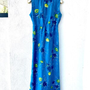 May include: A long blue sleeveless dress with a white crochet neckline and a floral print. The dress has a fitted bodice and a flowing skirt.