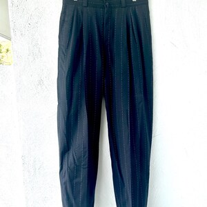 Peut inclure: Pantalon bleu marine fonc&eacute; avec un motif discret de fines rayures verticales. Ce pantalon pr&eacute;sente une taille haute avec des plis sur le devant, une fermeture &agrave; bouton et &agrave; glissi&egrave;re, des passants de ceinture et des ourlets &agrave; revers.