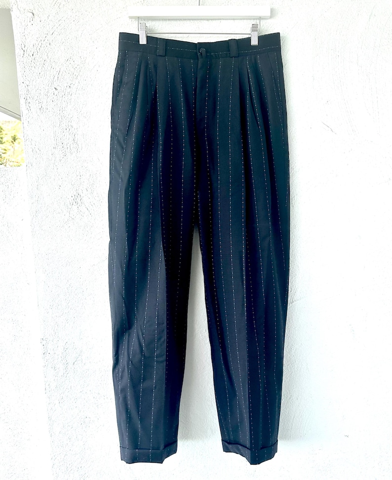 Peut inclure: Pantalon bleu marine fonc&eacute; avec un motif discret de fines rayures verticales. Ce pantalon pr&eacute;sente une taille haute avec des plis sur le devant, une fermeture &agrave; bouton et &agrave; glissi&egrave;re, des passants de ceinture et des ourlets &agrave; revers.