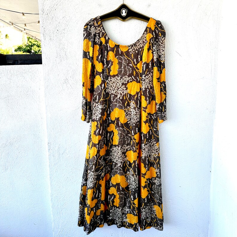 May include: A long-sleeved dress with a brown and yellow floral pattern. The dress has a scoop neck and a loose fit.