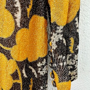 May include: A long-sleeved dress with a gold and black floral pattern. The dress has a sparkly texture and features buttons on the sleeves.