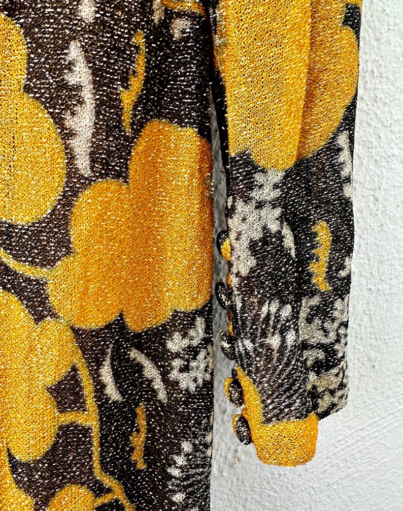May include: A long-sleeved dress with a gold and black floral pattern. The dress has a sparkly texture and features buttons on the sleeves.