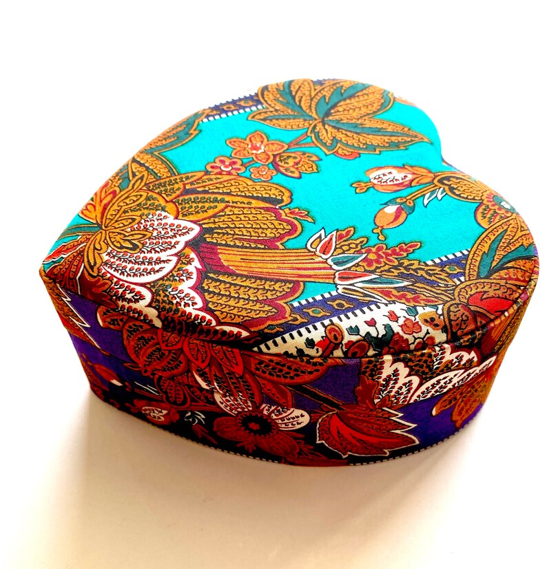 May include: A heart-shaped box with a colorful floral pattern. The box is made of fabric and has a blue, purple, and orange color scheme.