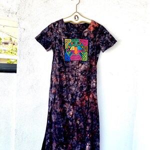 May include: A long, dark-colored dress with a tie-dye pattern. The dress has short sleeves and a square-shaped design on the front with colorful lines and a geometric pattern.