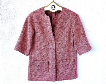 May include: A short-sleeved jacket in a speckled red and white textured fabric. The jacket features a round neckline, a front button closure with four visible buttons, and two large square patch pockets at the bottom front hem.