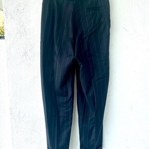Peut inclure: Un pantalon bleu marine fonc&eacute; orn&eacute; d'un discret motif &agrave; fines rayures blanches. Le pantalon pr&eacute;sente une ceinture structur&eacute;e avec des passants, une poche arri&egrave;re unique sur le c&ocirc;t&eacute; droit et des ourlets &agrave; revers au bas des jambes.
