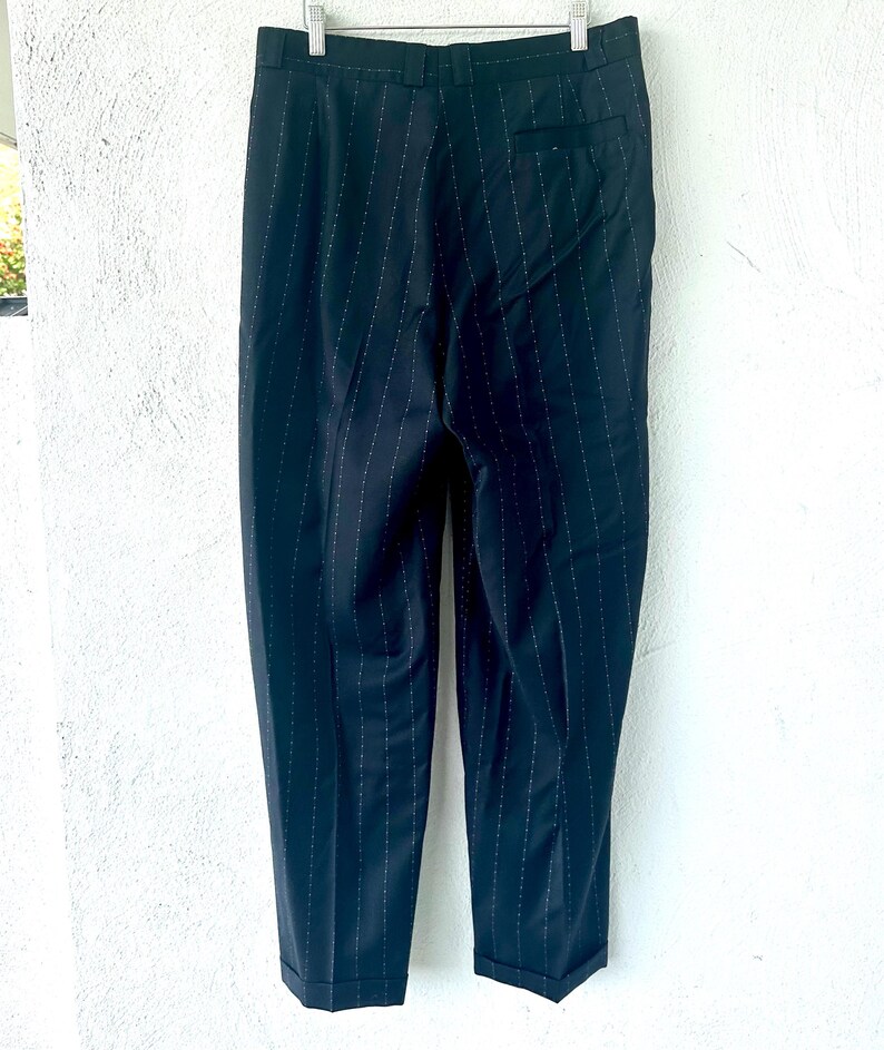 Peut inclure: Un pantalon bleu marine fonc&eacute; orn&eacute; d'un discret motif &agrave; fines rayures blanches. Le pantalon pr&eacute;sente une ceinture structur&eacute;e avec des passants, une poche arri&egrave;re unique sur le c&ocirc;t&eacute; droit et des ourlets &agrave; revers au bas des jambes.
