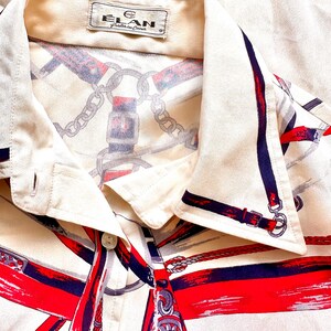 May include: A white button-down shirt with a red, blue, and white equestrian-themed print. The shirt has a collar and a button closure. The label on the shirt reads "Elan, Crafted in China."