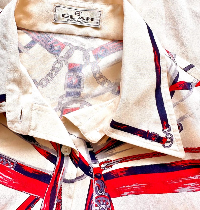 May include: A white button-down shirt with a red, blue, and white equestrian-themed print. The shirt has a collar and a button closure. The label on the shirt reads "Elan, Crafted in China."