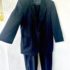 Peut inclure: Un costume bleu marine fonc&eacute; avec un motif &agrave; fines rayures blanches. L'ensemble comprend un blazer simple boutonnage &agrave; revers crant&eacute;s, manches longues et deux poches avant, assorti &agrave; un pantalon avec un ourlet &agrave; revers au bas des jambes.