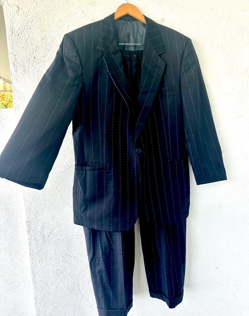 Peut inclure: Un costume bleu marine fonc&eacute; avec un motif &agrave; fines rayures blanches. L'ensemble comprend un blazer simple boutonnage &agrave; revers crant&eacute;s, manches longues et deux poches avant, assorti &agrave; un pantalon avec un ourlet &agrave; revers au bas des jambes.