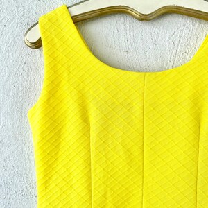 Pu&ograve; includere: Un abito giallo senza maniche con un motivo a rombi. L'abito ha una scollatura rotonda ed &egrave; realizzato in un tessuto strutturato.